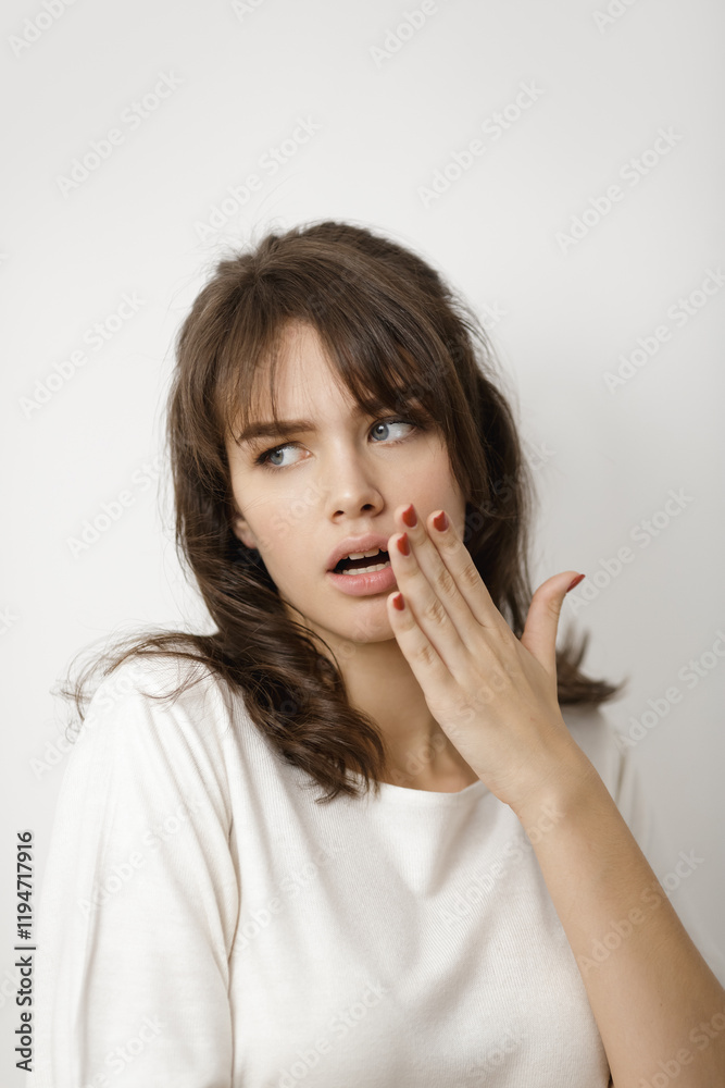 Portrait of a young Caucasian woman in a casual white top, covering her mouth with her hand and expressing surprise. Perfect for lifestyle, emotions, or reaction-based editorial projects. Portrait of a young Caucasian woman in a casual white top, covering her mouth with her hand and expressing surprise. Perfect for lifestyle, emotions, or reaction-based editorial projects.