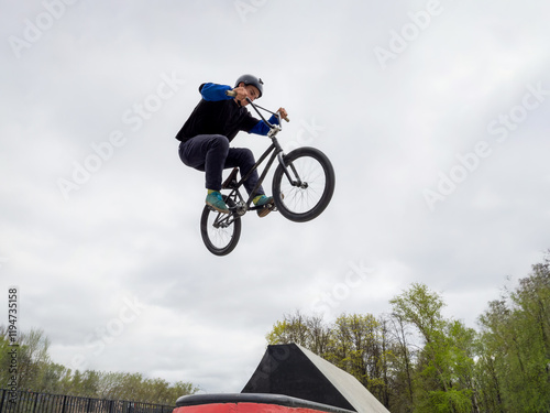 BMX bicycle rider doing stunt jump over spinу in quarter pipe. Skilled BMX freestyler athlete jumping over quarter ramp and doing aerial trick Tailwhip in street ramp park outdoors photo