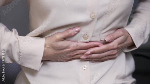 Close up. Female hands holding massaging stomach. Businesswoman feels stomach pain while sitting at workplace in business office. Sick woman suffers from gastritis, menstruation, poisoning or bloating