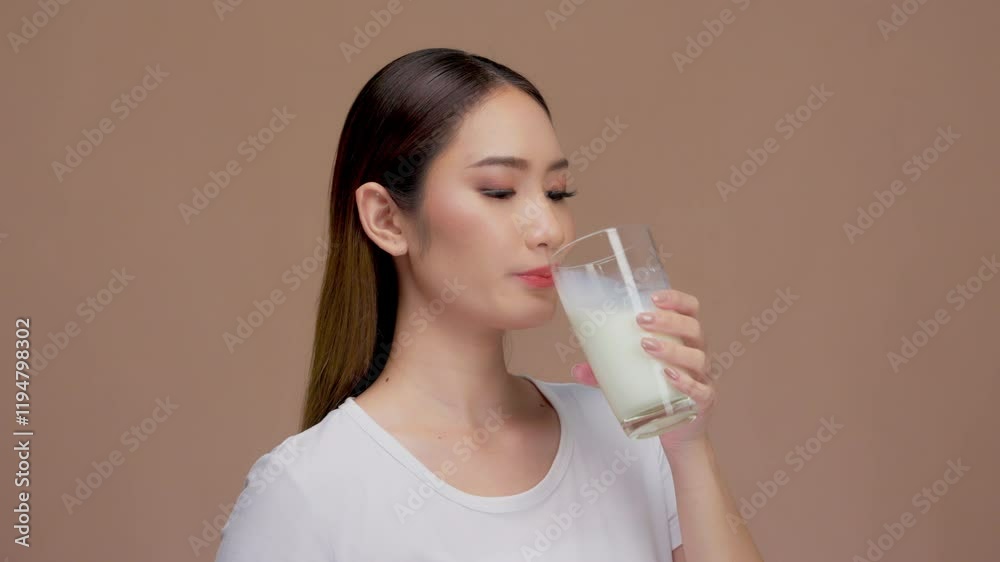 Happy young asian woman drinking a glass of milk or water on a solid background Happy young asian woman drinking a glass of milk or water on a solid background