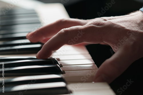 A man is playing the piano, hands on the keys in close-up, the background is blurred.
