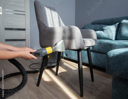 A girl s hand with a washing vacuum cleaner cleans the gray upholstery of a fabric chair in the apartment from dirt. Cleaning services, upholstered furniture cleaning photo