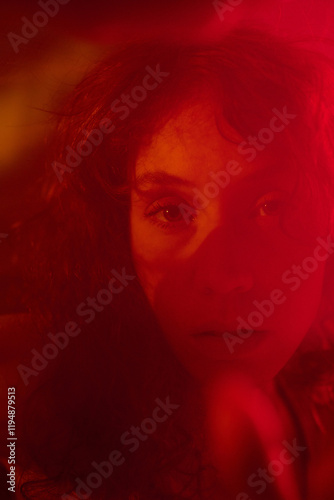 Vertical shot of attractive face of young adult woman sitting under veil illumed with red neon light photo