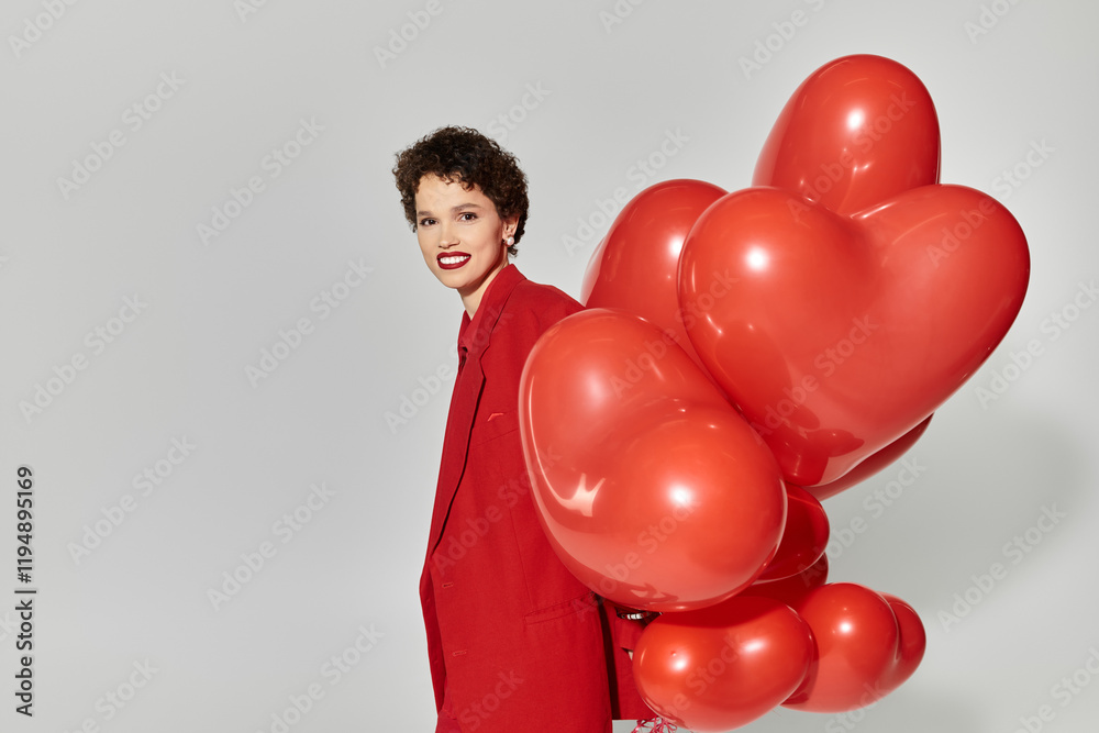 Joyful young woman in vibrant red attire holding heart shaped balloons in a stylish studio Joyful young woman in vibrant red attire holding heart shaped balloons in a stylish studio