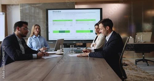 Two parties represented by business professionals reviewing, signing contract at conference table during negotiation, shake hands as gesture of mutual respect, finalize successful completion of deal