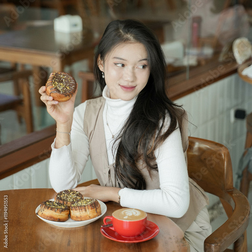 Young Beautiful Asian lady sitting in the coffee shop, showing pastry, a cup of coffee