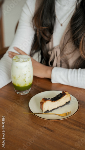 Closeup photography of a cheese cake and beautiful Asian women with long hair on wooden table in coffee shop.