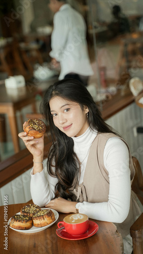 Young Beautiful Asian lady sitting in the coffee shop, showing pastry, a cup of coffee