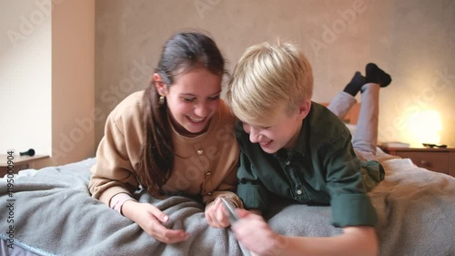 A brother and sister sit together, using their smartphones and laughing as they share funny videos or messages, enjoying their time together.