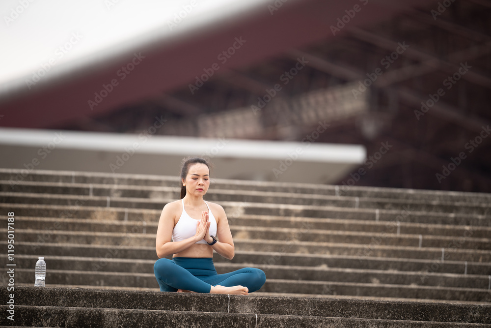 Obraz premium A woman is sitting on a set of stairs, meditating. Concept of calm and tranquility, as the woman focuses on her breathing and clears her mind. The setting of the stairs adds a sense of elevation