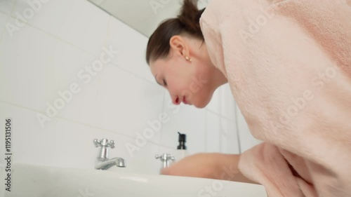 Woman washing face in sink. Female cleansing skin with water at bathroom basin. Lady rinsing face at washbasin. Person refreshing skin with cool water in restroom
