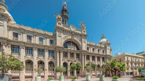 Historic Post Office (Palau de les Comunicacions) in Valencia timelapse hyperlapse at City Hall Square (Plaza del Ayuntamiento). Ornate facade, traffic and a blue sky in the Spanish city center. photo