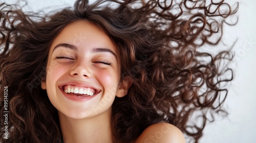 Joyful expression and natural curly brown hair spread out against white background showcasing genuine happiness and carefree spirit in beauty and lifestyle portrait