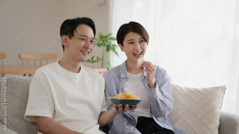 リビングでポテトチップスを食べる笑顔の日本人男女 リビングでポテトチップスを食べる笑顔の日本人男女