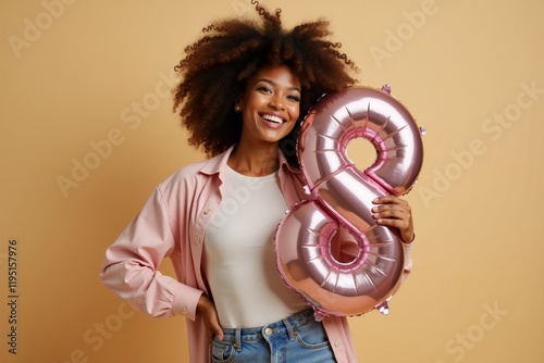 Young woman joyfully holding a pink balloon shaped like number eight on a plain background to celebrate International Women's Day photo