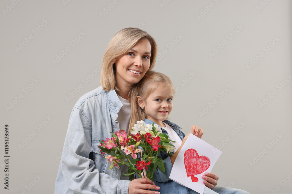 Happy woman with her daughter, bouquet of alstroemeria flowers and greeting card on gray background. Mother's Day celebration Happy woman with her daughter, bouquet of alstroemeria flowers and greeting card on gray background. Mother's Day celebration