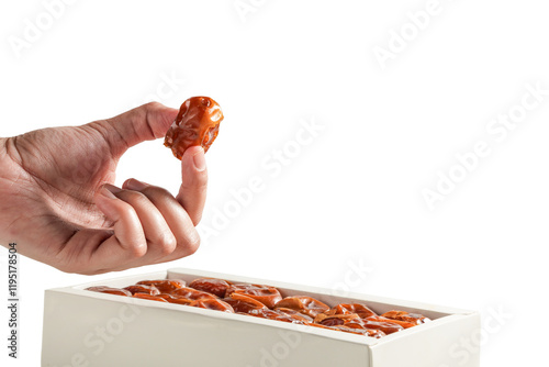 A hand picking a Sukari date from a white box, isolated on a white background photo