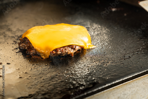 A melted slice of cheddar cheese on top of a grilled beef patty