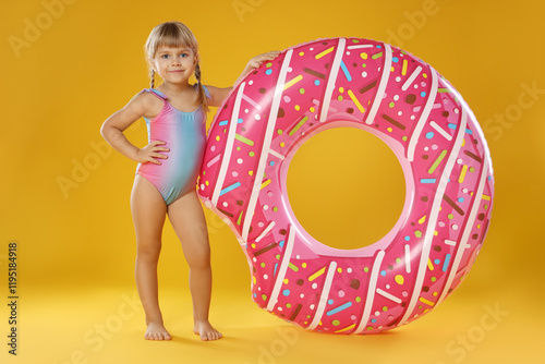Cute little girl in swimsuit with inflatable ring on orange background
