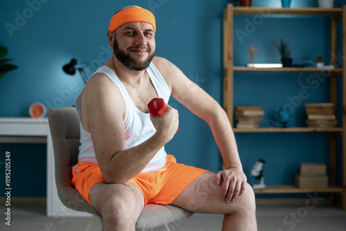 Funny bearded bald man wearing orange shorts making fitness training with dumbbells in the living room at home. Active lifestyle and training at home photo