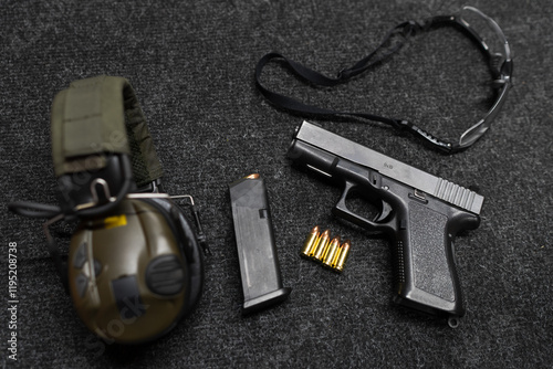 A pistol with a magazine and cartridges, active headphones and protective glasses on a table in a shooting range.