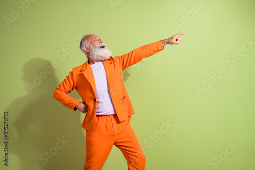 Photo of funny showman indicate finger empty space wear orange suit isolated on green color background photo