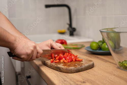 Man cutting red pepper on a wooden chopping board in the kitchen.