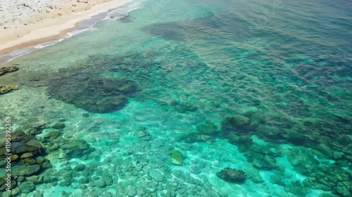 Aerial view of a serene beach with clear turquoise waters and rocky shoreline.