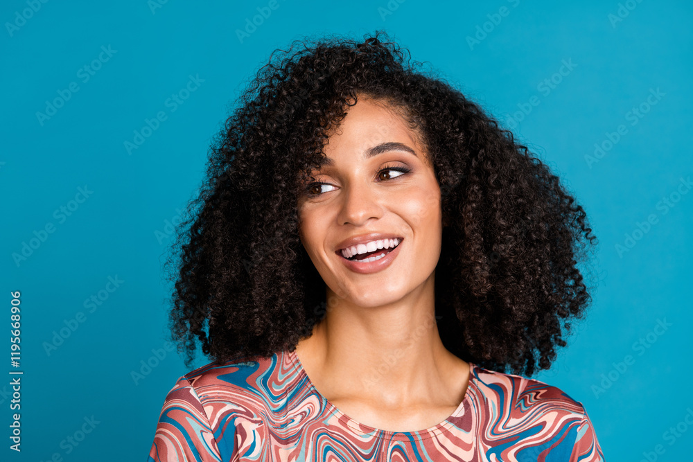 Smiling young woman with curly hair, wearing a trendy print t-shirt, poses against a bright blue background Smiling young woman with curly hair, wearing a trendy print t-shirt, poses against a bright blue background