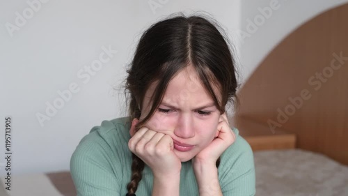Portrait of sad preteen girl sitting on bed at home. Depressed child having bad mood. Kid feeling upset and lonely