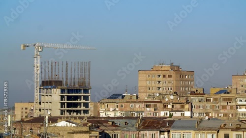 Wallpaper Mural Time Lapse video. A moving crane works above an unfinished building surrounded by residential structures under a blue sky. Torontodigital.ca