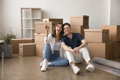 Portrait of young 30s Hispanic homeowners family showing bunch of keys from new house, sit on floor laughing, look at camera, celebrate housewarming, first day at their new flat. Bank loan, tenancy