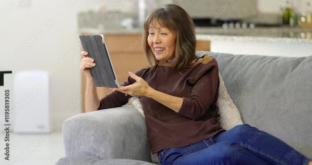 Happy woman sitting on home sofa enjoying talking by mobile tablet video chat Happy woman sitting on home sofa enjoying talking by mobile tablet video chat