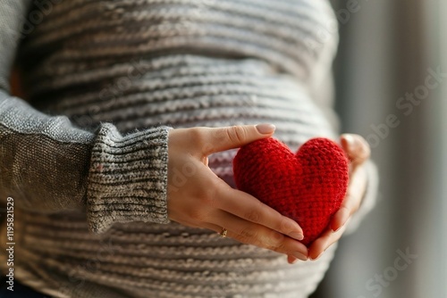 close-up shot of a woman's hand holding a red heart, with focus on the midsection area. The image can symbolize concepts related to cancer, pregnancy, and health. photo