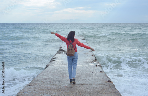 Obraz na płótnie Rear view of a young woman tourist with a backpack standing on the pier and waves hitting the pier in a storm. City of Sudak, Crimea. w salonie