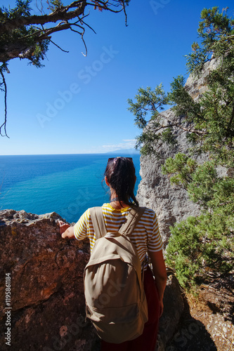Obraz na płótnie A young female traveler with a backpack sits on the top of Karaul-Oba mountain, Novy Svet village, Crimea, enjoying the sea view. A tourist with a backpack travels through the Crimea w salonie