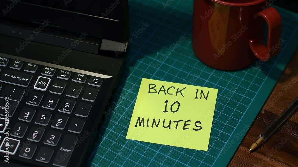Man’s hand sticking yellow Back in 10 minutes note message to office desk mood lighting copy space