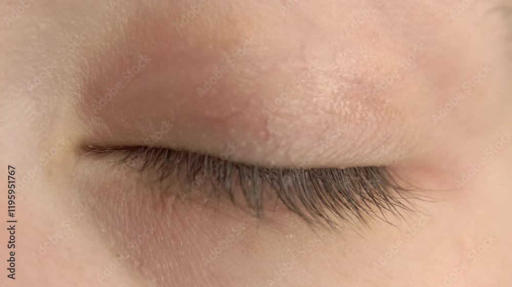 A close-up video of a woman's closed eye slowly opening, showcasing eyelashes, eyelid details, and subtle skin textures in a natural and intimate perspective