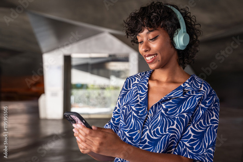 Latin woman with headphones smiling at phone in modern setting photo