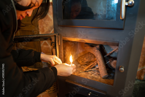 Asian woman lighting a fire in a wood burning stove