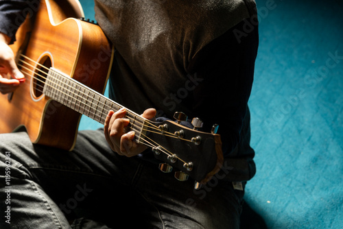 Skilled musician playing acoustic guitar in a dark room illuminated by a dim light