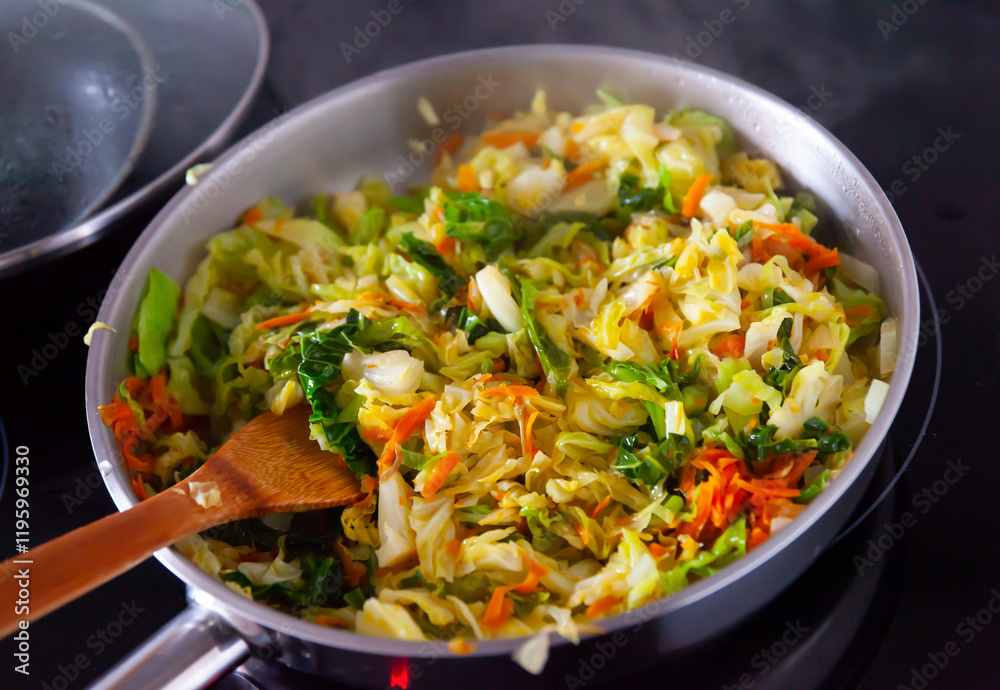 Chopped cabbage braising with vegetables in open pan. Wooden spatula for stirring. Chopped cabbage braising with vegetables in open pan. Wooden spatula for stirring.