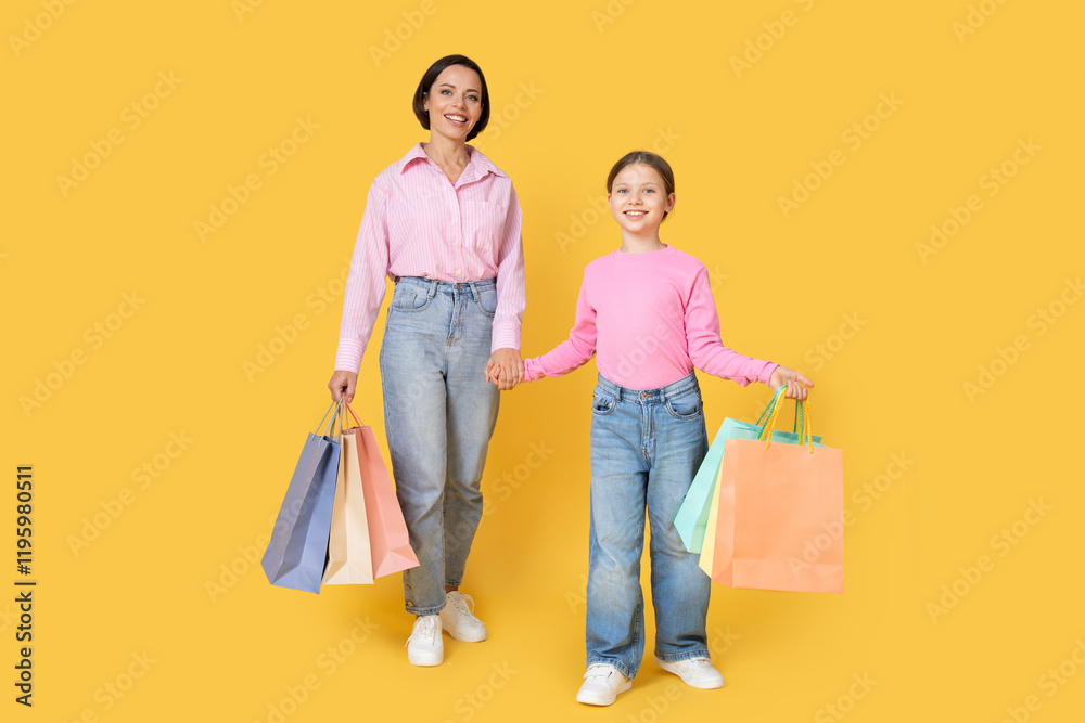 A mother and her preteen daughter are smiling and holding hands while carrying shopping bags. They share a joyful moment together against a vibrant yellow background, celebrating their day out. A mother and her preteen daughter are smiling and holding hands while carrying shopping bags. They share a joyful moment together against a vibrant yellow background, celebrating their day out.