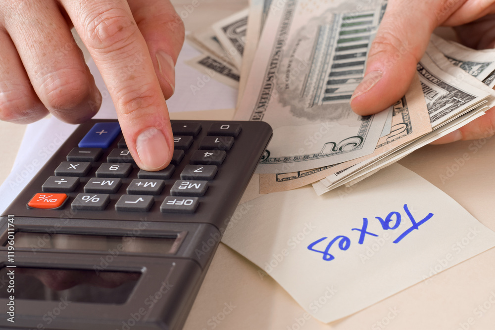 Closeup person's hand using calculator counting american money doing taxes Closeup person's hand using calculator counting american money doing taxes