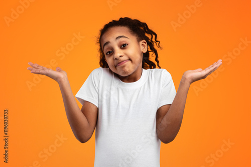 Funny Clueless African American Girl Shrugging Shoulders Gesturing I Don't Know Posing Standing Over Orange Yellow Background In Studio, Looking At Camera. Shoulder Shrug Concept