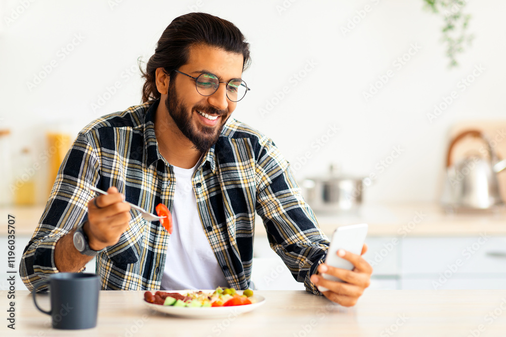 Handsome young arab long-haired, bearded man using cellphone while having healthy and tasty breakfast, checking social media or watching funny videos online, sitting at kitchen alone, copy space Handsome young arab long-haired, bearded man using cellphone while having healthy and tasty breakfast, checking social media or watching funny videos online, sitting at kitchen alone, copy space