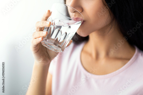 Young Indian woman drinking clear mineral water from glass at home, selective focus. Lovely Hindu lady staying hydrated, taking care of her body. Healthy living and detox concept photo