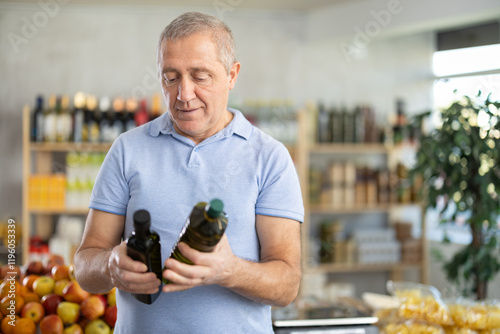 Canvas Print Concerned old man deciding between kinds of olive oil in the supermarket