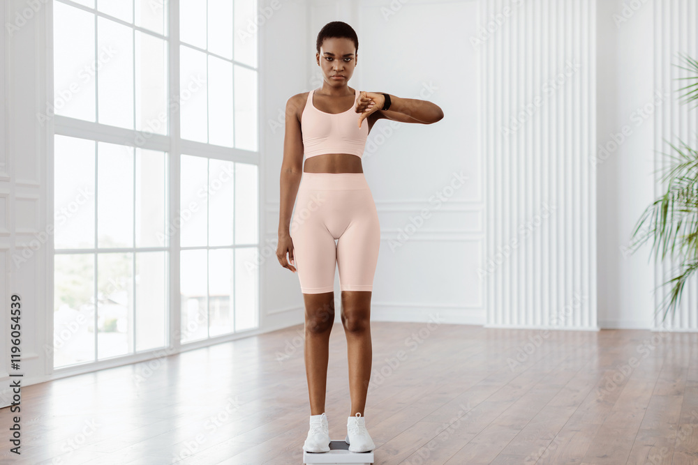 Fototapeta premium Full Body Length Of Sad And Disappointed African American Woman Standing On Bathroom Scales, Unhappy About Her Body Parameters, Showing Thumb Down Sign Gesture. Slimming Fail, Unsuccessful Weight Loss