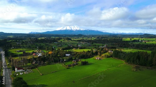 Aerial View of a Countryside Village with Green Pastures and Snow-Capped Mountain